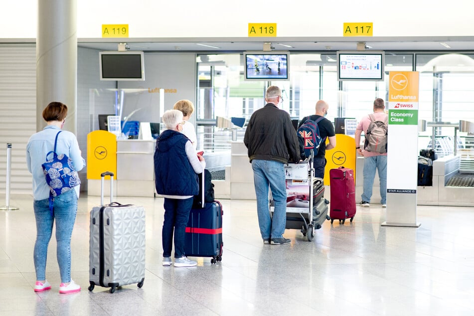 Fluggäste stehen mit ihrem Gepäck vor einem Check-in-Schalter in der Abflughalle des Flughafens Hannover.