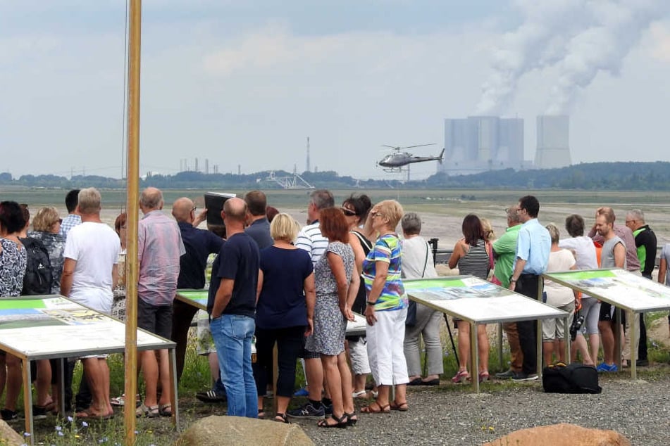 Am Aussichtspunkt des Tagebaus Vereinigtes Schleenhain sehen Schaulustige der Hubschrauberbesatzung bei der Arbeit zu.
