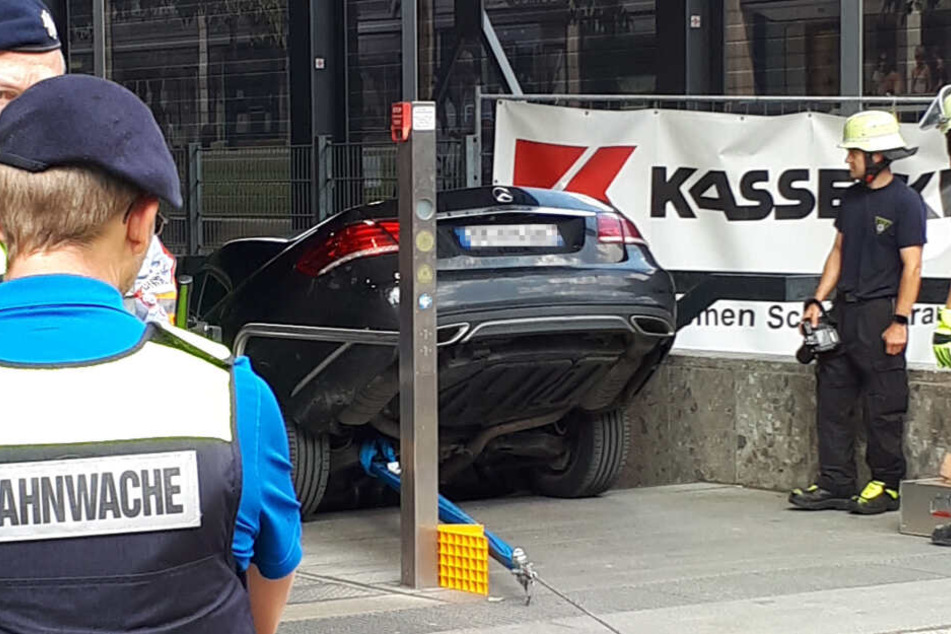Einsatzkräfte der Feuerwehr betrachten einen Mercedes, der die Treppe eines U-Bahn-Eingangs in München hinuntergefahren ist.
