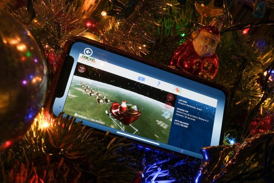 A cell phone with NORAD's Santa Tracker on screen is shown nestled in a Christmas tree.