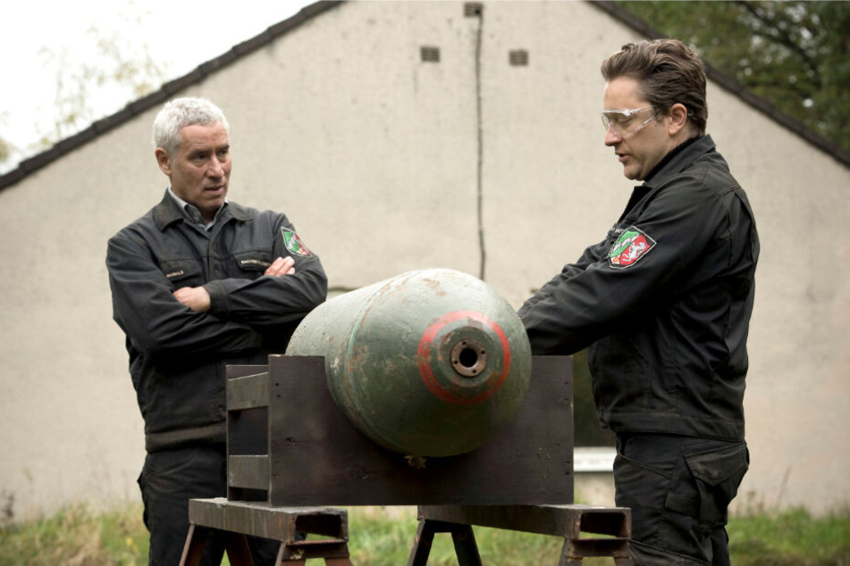 Maiwald (Ralph Herforth,, li.), der Leiter der Dienststelle des Kampfmittel-Räumdienstes, und sein Sohn und Kollege Joachim (Adrian Topol) üben mit einer Bomben-Attrappe.