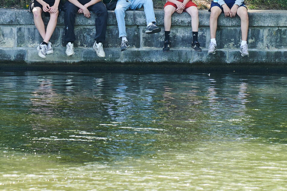 Fünf junge Männer sitzen bei fast 30 Grad Lufttemperatur auf einer Mauer am Landwehrkanal. (Symbolbild)
