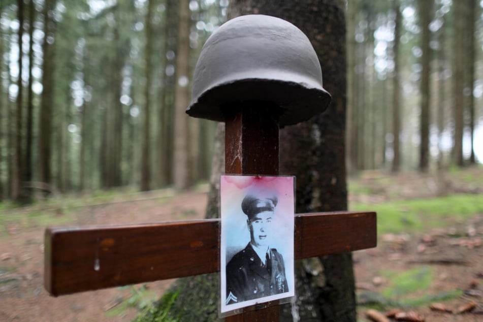 Ein Kreuz mit Helm und dem Bild eines gefallenen, amerikanischen Soldaten steht am Ochsenkopf im Hürtgenwald.