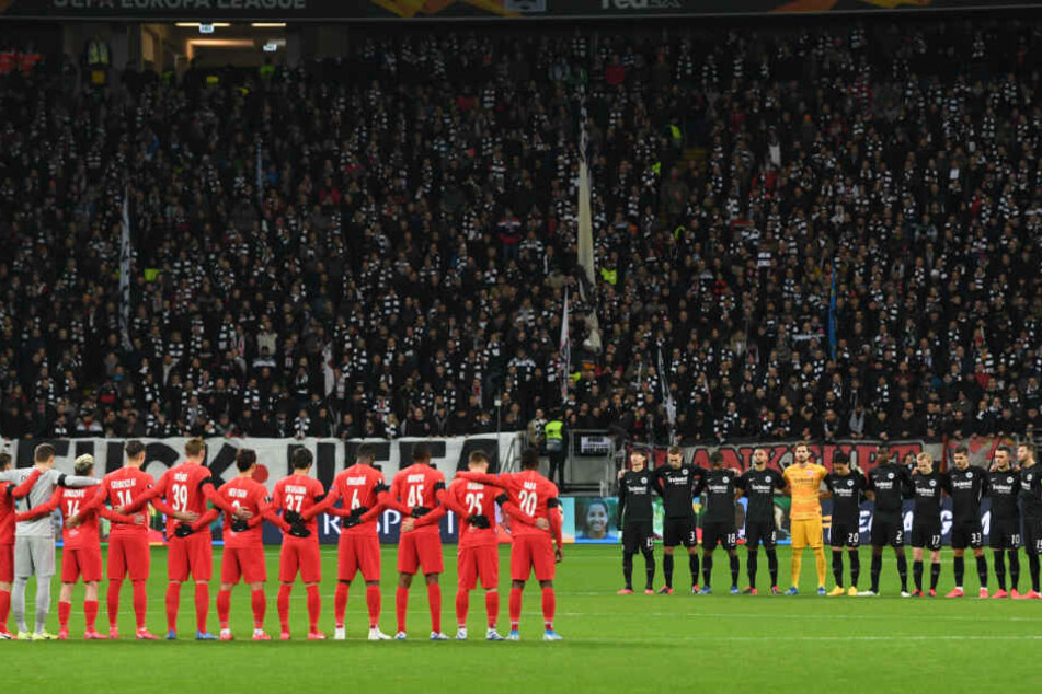 Die Spieler von Eintracht Frankfurt (r) und RB Salzburg stehen bei einer Schweigeminute für die Opfer des Anschlags in Hanau zusammen.