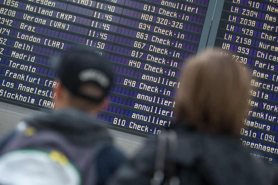 Reisende stehen vor einer Abflugtafel im Flughafen in München.