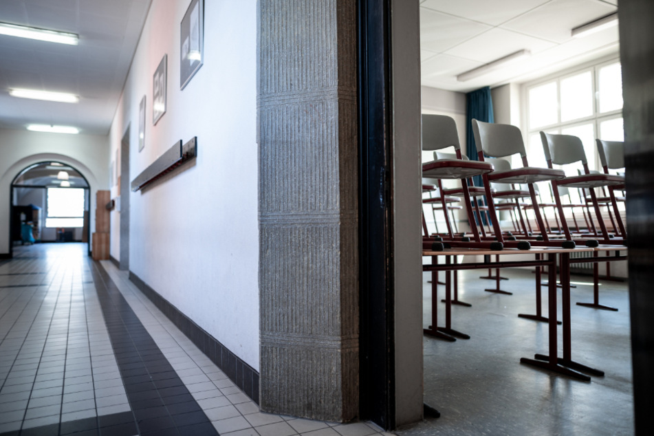 Oberhausen: Stühle stehen auf den Tischen in einem Klassenzimmer, daneben ist der leere Flur der Schule zu sehen.