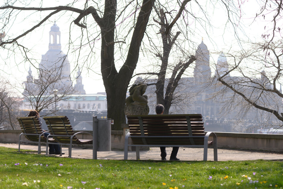 Passanten sitzen am Ufer der Elbe vor der Kulisse der Altstadt mit der Frauenkirche (l.) und dem Ständehaus auf einer Bank.