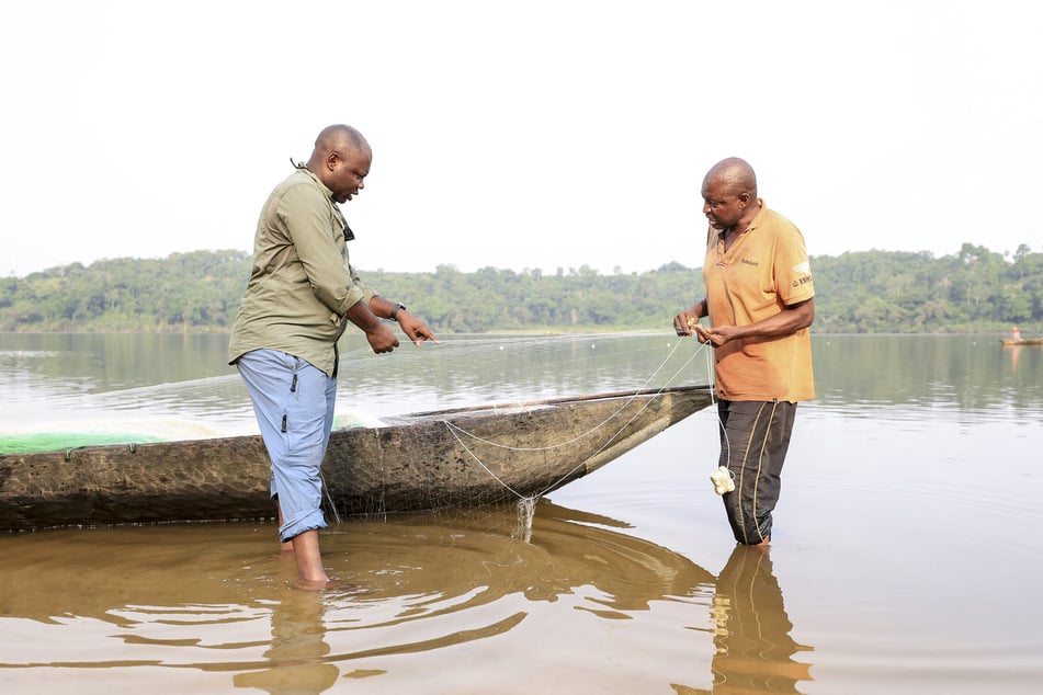 Aristide Takoukam Kamla (l.), a marine biologist specializing in the African manatee, talks with a fisherman in Dizangue, on December 11, 2024.