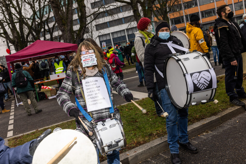 Freiburg am Samstag: Teilnehmer einer Demo gegen die Corona-Maßnahmen stehen auf dem Fahnenbergplatz und trommeln, während sie Schilder mit Slogans tragen.