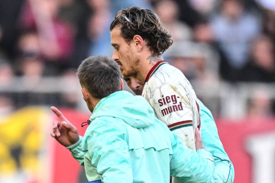 Augsburgs Calvin Brackelmann wird benommen von Betreuern vom Platz geführt.