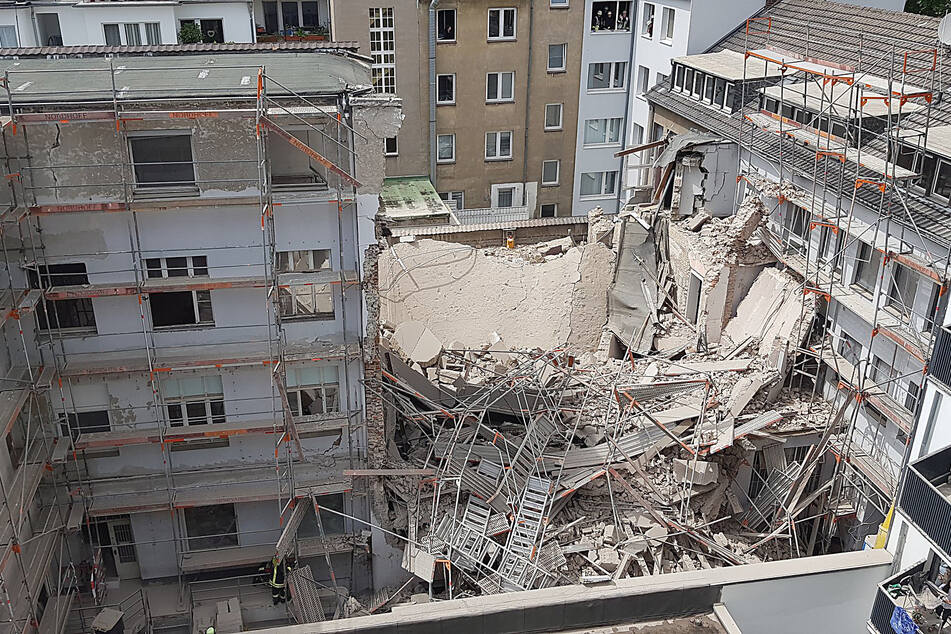 Einsatzkräfte der Feuerwehr stehen vor einer Hauseinfahrt, durch die ein eingestürztes Gerüst zu sehen ist.