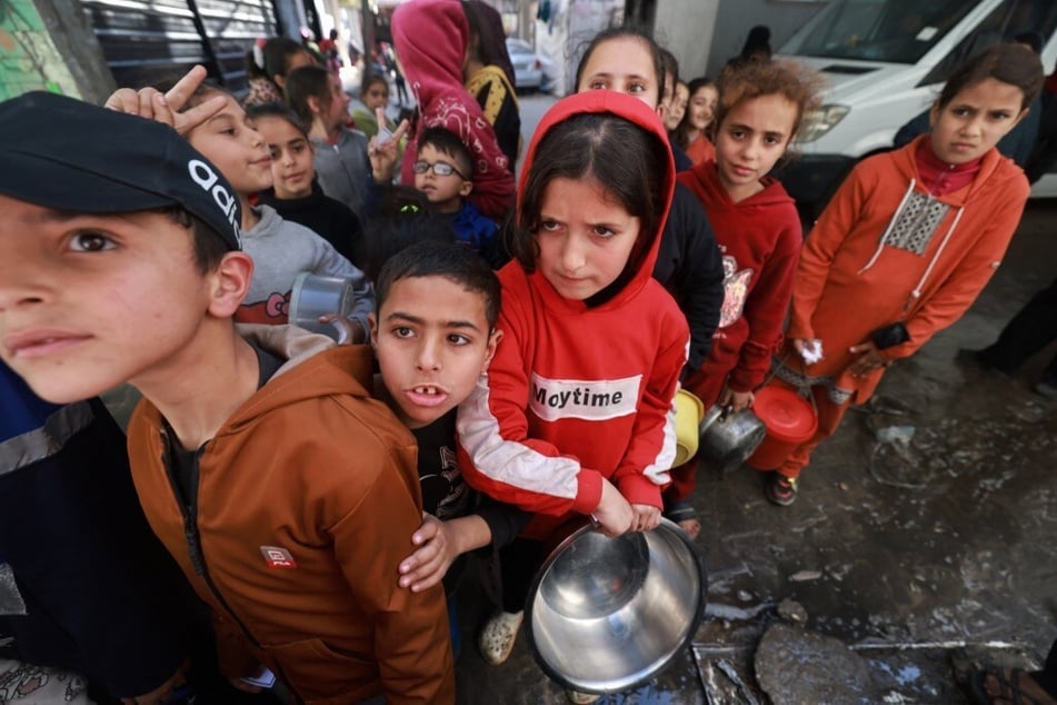 Palestinian children receive cooked food rations as part of a volunteer youth initiative in Rafah in the southern Gaza Strip