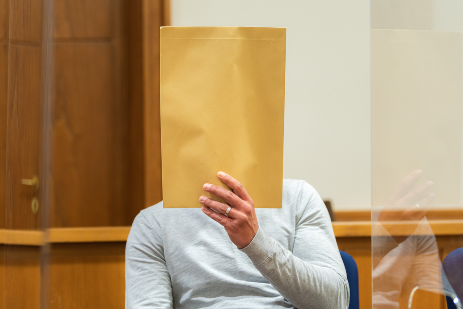 Der 33-Jährige sitzt mit einem Umschlag vor dem Gesicht in einem Gerichtssaal des Landgerichts Oldenburg.