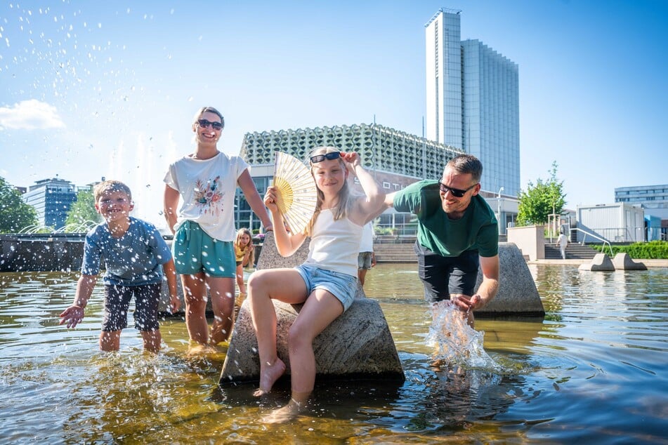 Emily (10, 3.v.l.) kühlt sich zusammen mit Bruder Jona (7), Mama Anne-Katrin (35) und Papa Michael (36) die Füße im Stadthallenbrunnen.