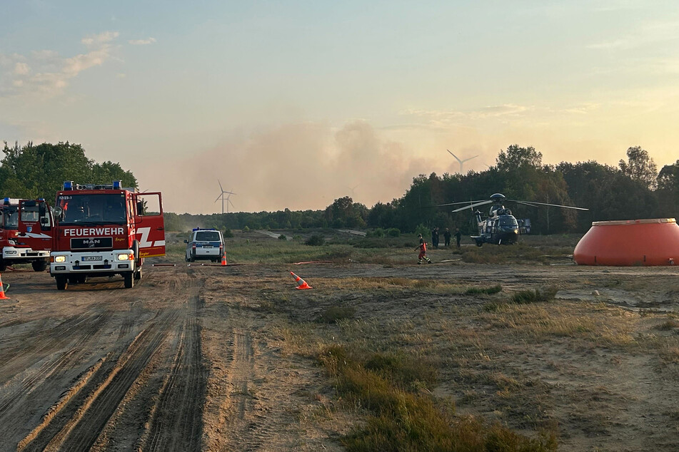 Feuerwehrkräfte sind neben einem Löschhubschrauber in einem Waldstück nahe Jüterbog im Einsatz. Inzwischen hat sich die Lage vor Ort beruhigt.