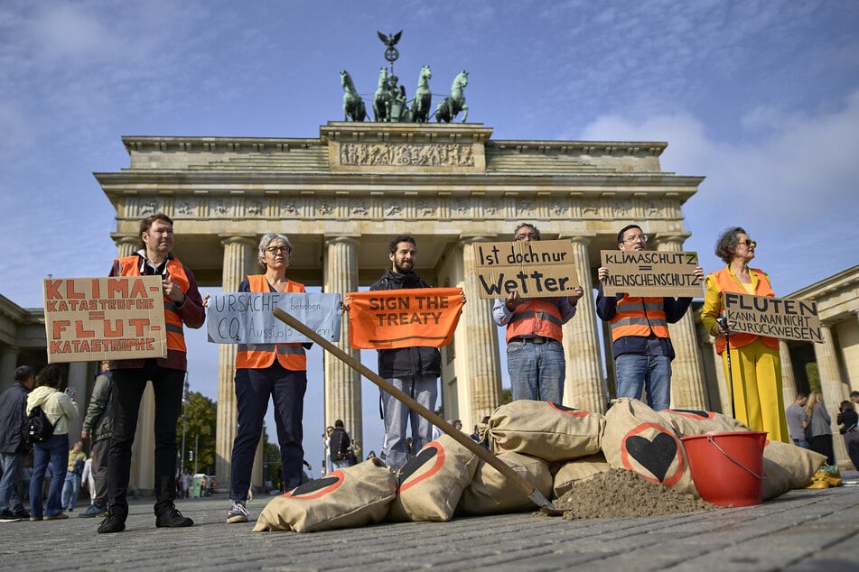 Mitglieder der "Letzten Generation" stehen mit Plakaten und Sandsäcken vor dem Brandenburger Tor und protestieren gegen den Klimawandel.