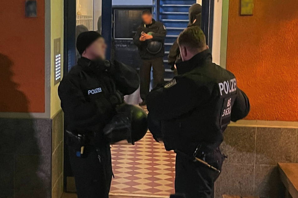 Polizeibeamte stehen am Eingang zu dem Gebäude in der Grünberger Straße, in dem eine Wohnung durchsucht worden ist.
