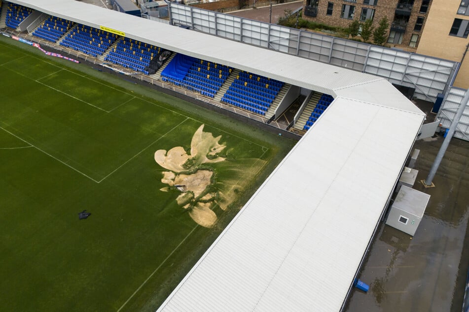 Ein Erdloch auf dem Spielfeld und überflutete Gehwege im Cherry Red Records Stadium, der Heimstätte des AFC Wimbledon.