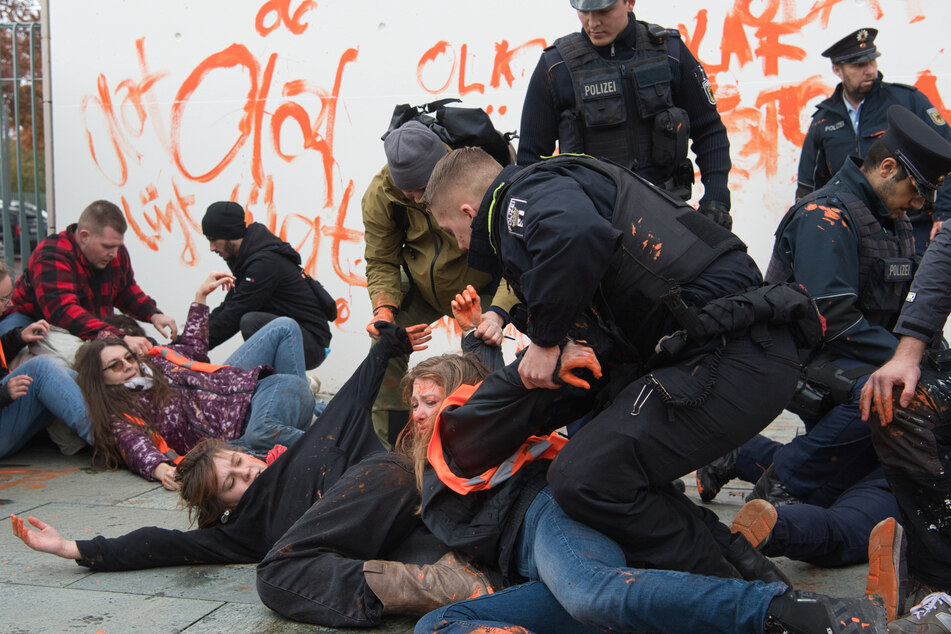 Klimaaktivisten der "Letzten Generation" haben die Wände des Bundeskanzleramts beschmiert und werden von Polizisten festgehalten.