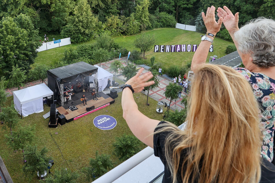 Fans der Band Karat verfolgen von der Dachterrasse ihrer Suite aus ein Hotelzimmer-Konzert im Garten des Hotels.