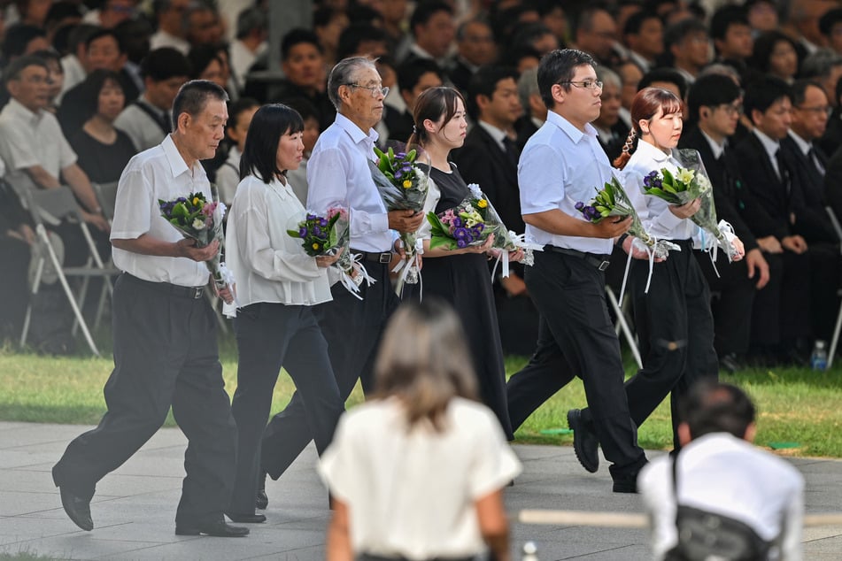 Invited guests carry bouquets of flowers to lay at the Memorial Cenotaph during the Peace Memorial Ceremony to mark the 80th anniversary of the world's first atomic bomb attack, in the city of Hiroshima on Wednesday.