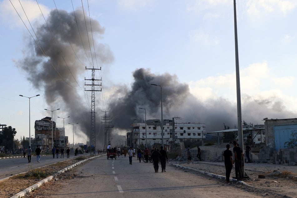 Smoke plumes rise during an Israeli strike as people walk along the Salah al-Din road near the Nuseirat refugee camp in the central Gaza Strip, used by Palestinians to reach an aid distribution point set up by the privately-run Gaza Humanitarian Foundation, on June 25, 2025.