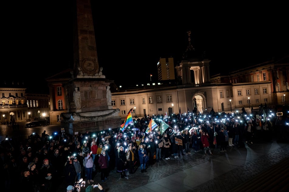 Bei einer Demo in Potsdam zeigen etliche Menschen Flaggen und Licht gegen rechte Politik.