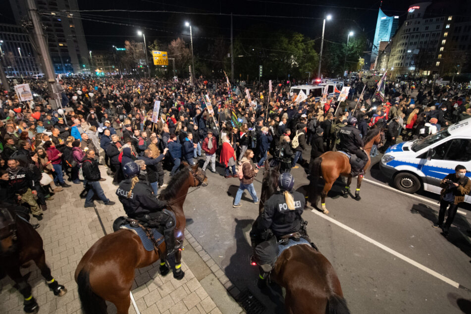Teilnehmer stehen nach dem Ende einer Demonstration der Stuttgarter Initiative "Querdenken" am Hauptbahnhof Leipzig hinter der Reiterstaffel der Polizei.