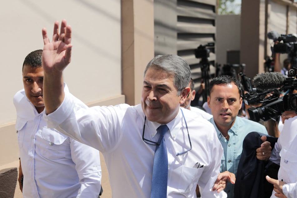 Former Honduran President Juan Orlando Hernandez waves as he walks outside the Supreme Court after appearing before a judge on fraud and money-laundering charges in Tegucigalpa on August 3, 2026.