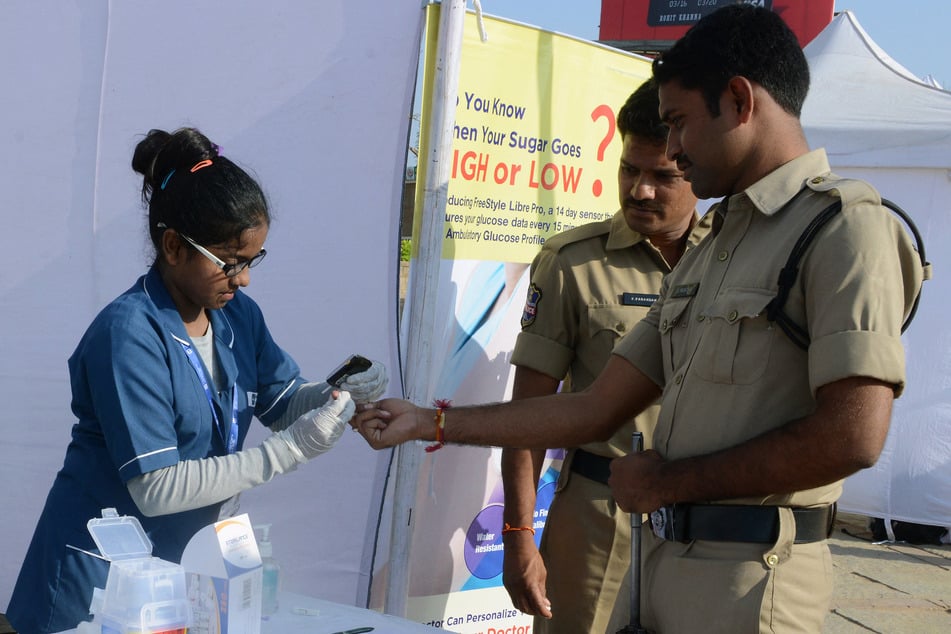 An Indian nurse (l.) collects a blood sample from police using a glucometer at a free diabetic health check-up camp on World Health Day in Hyderabad on April 7, 2016.