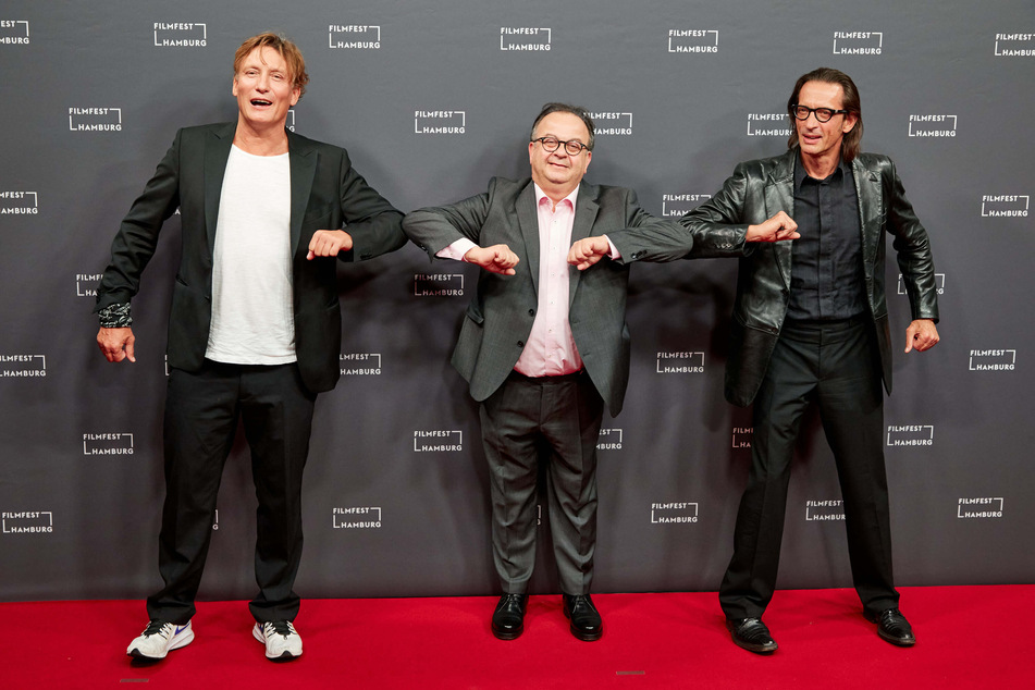 Oliver Masucci (l.-r.), Schauspieler, Albert Wiederspiel, Leiter des Filmfestes, und Oskar Roehler, Regisseur, stehen auf dem Roten Teppich zur Eröffnung des Filmfestes Hamburg.