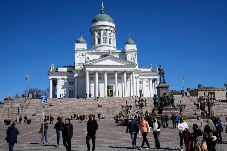Menschen gehen vor dem Dom von Helsinki unter blauem Himmel im Stadtzentrum entlang.