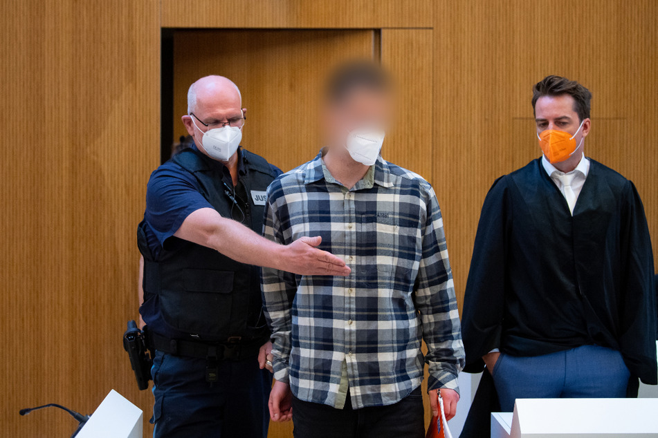 Einer von zwei wegen Mordes angeklagten Männer (M) wird vor Beginn der Verhandlung in den Sitzungssaal geführt. Rechts steht sein Anwalt Alexander Stevens.