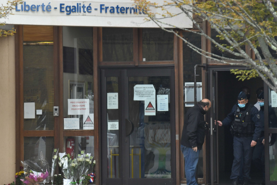 Die französische CRS-Polizei (Compagnies Republicaines de Securite) verlässt eine Mittelschule in Conflans Saint-Honorine, 30 km nordwestlich von Paris, neben Blumen, die nach einer brutalen Messerattacke ausgestellt wurden
