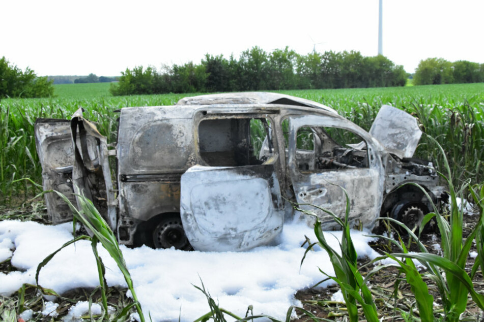 Das ausgebrannte Auto steht in einem Feld, umgeben von Löschschaum.