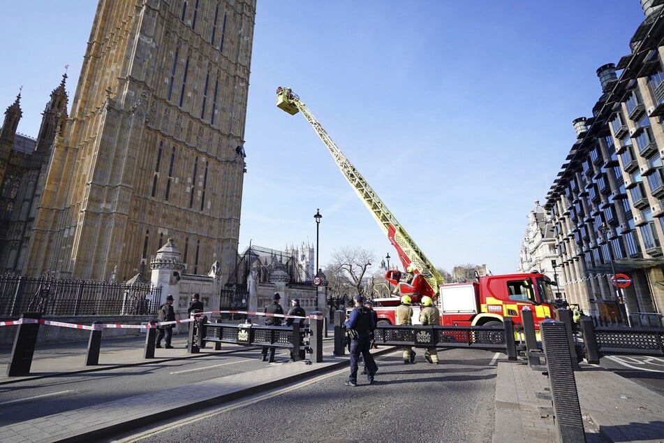 Feuerwehrleute nähern sich mit einem Korb einem Mann, der mit einer Palästina-Flagge auf einem Mauervorsprung des Elizabeth Towers sitzt.