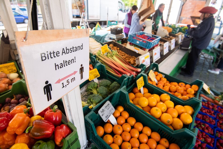 Ein Schild "Bitte Abstand halten" hängt bei einem Obst- und Gemüsehändler auf einem Wochenmarkt.