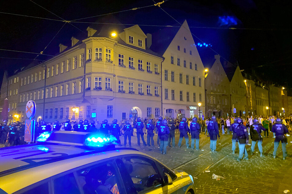 Polizisten stehen an einem Platz in der Innenstadt, wo sich Menschen zum Feiern versammelt haben.