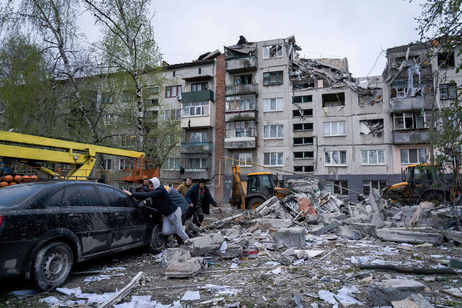 Anwohner schieben ein beschädigtes Auto vor einem getroffenen Gebäude in Slowjansk. Kurz vor dem orthodoxen Osterfest amheutigen Sonntag ist die Ukraine erneut von einem schweren russischen Raketenangriff erschüttert worden.