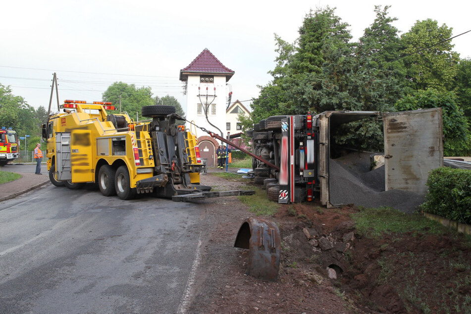 Der Lkw liegt auf der Seite. Das geladene Kies liegt größtenteils im Vorgarten eines Wohnhauses.