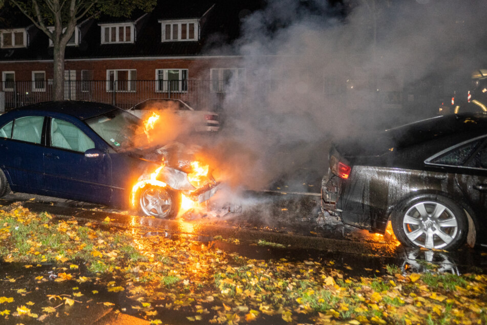 Ein Auto brennt im Motorbereich, Feuerwehrleute eilen herbei.