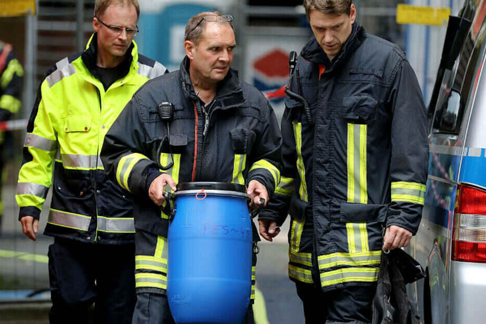 in Feuerwehrmann trägt vor dem Wohnkomplex in Köln-Chorweiler eine Tonne mit Gift heraus.
