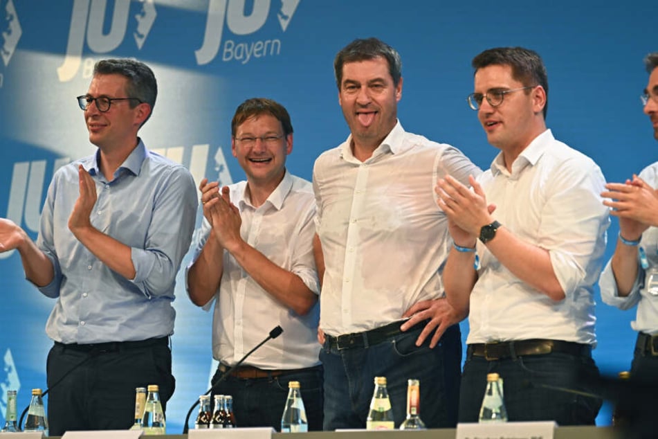 Markus Söder (CSU, M), Ministerpräsident von Bayern, steht nach seiner Rede mit durchgeschwitztem Hemd auf der Bühne und streckt aufgrund der warmen Temperaturen die Zunge heraus.