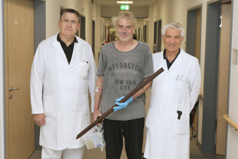 Frank Vaorin (55, M.) posiert mit seinen behandelten Ärzten und der Zaunstange, die ihn nach einem Sturz praktisch längs aufspießte.