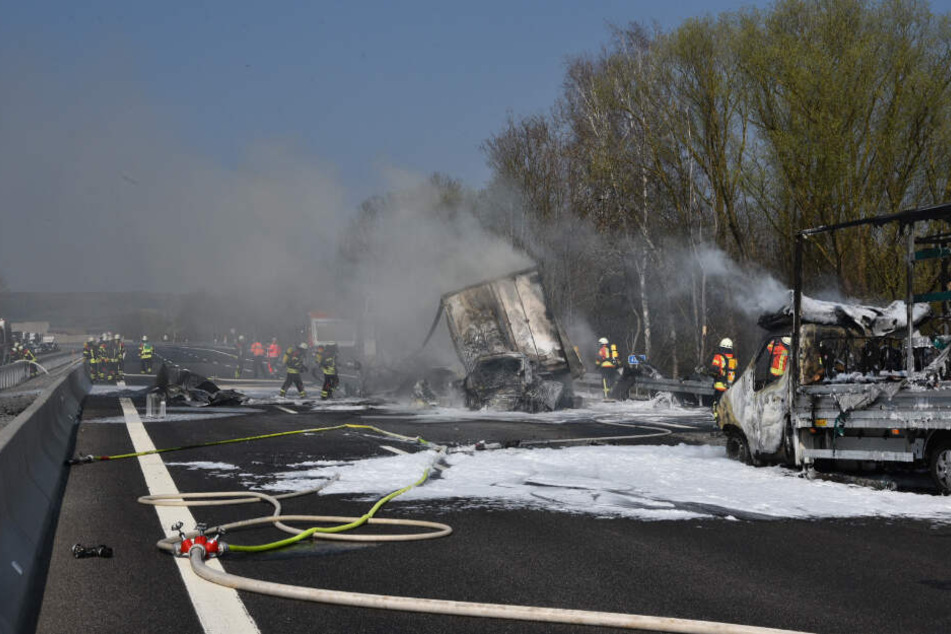 Einsatzkräfte an der Unfallstelle neben ausgebrannten Fahrzeugen.