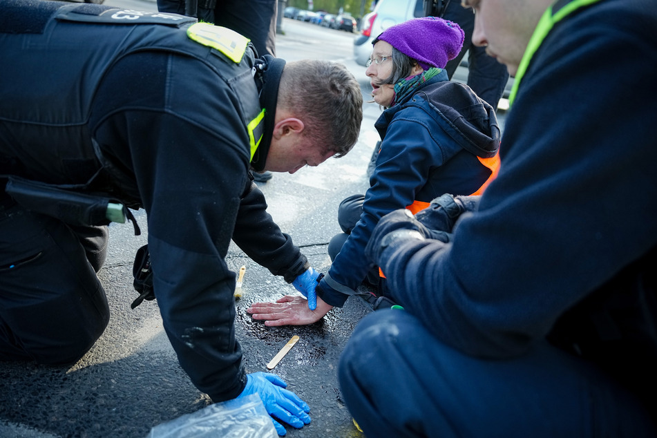 Ein Polizeibeamter löst die Hand einer Klimaaktivistin von der Straße.