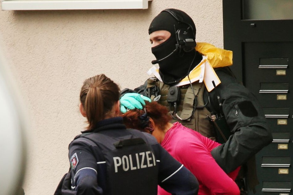 Die 50-jährige Frau wird von Polizisten aus dem Haus geführt.