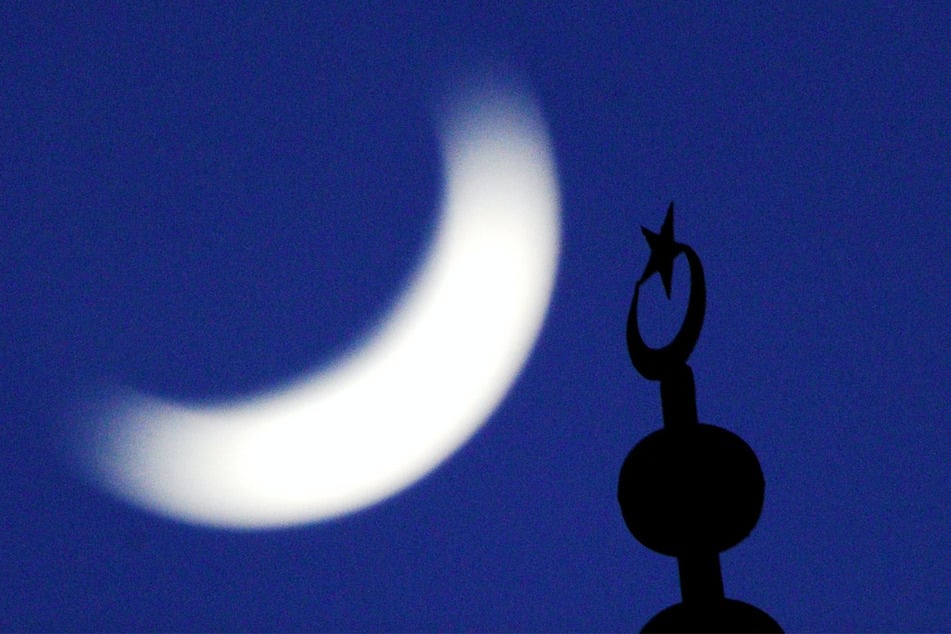 Die Spitze eines Minaretts steht vor dem am Himmel stehenden Halbmond. (Symbolbild)