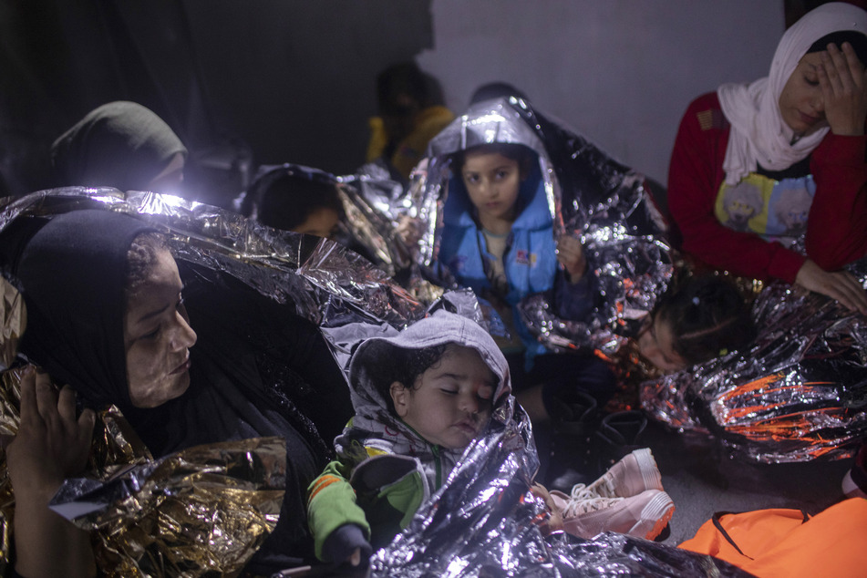 Migranten sitzen in Thermodecken gehüllt auf einem Schiff der griechischen Küstenwache. (Archivbild)