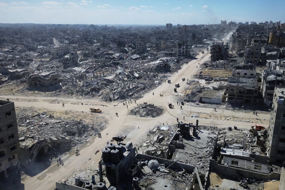 Palästinenser gehen über eine Kreuzung in Gaza, die von zerstörten Gebäuden umgeben ist.